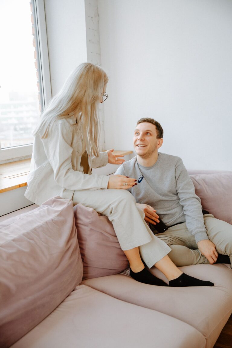 Couple sitting closely on a couch, engaged in an emotional, warm conversation with natural window light