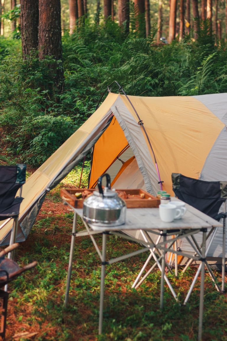 Cozy camping scene with tent, chairs, and table in a lush forest. Ideal for outdoor adventure enthusiasts.