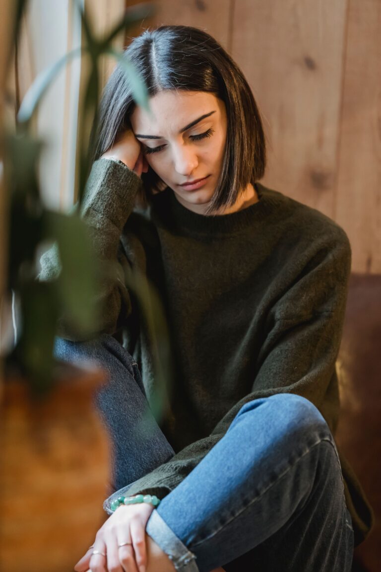A woman sits alone near a sunlit window with her eyes closed, taking a quiet break from dating.