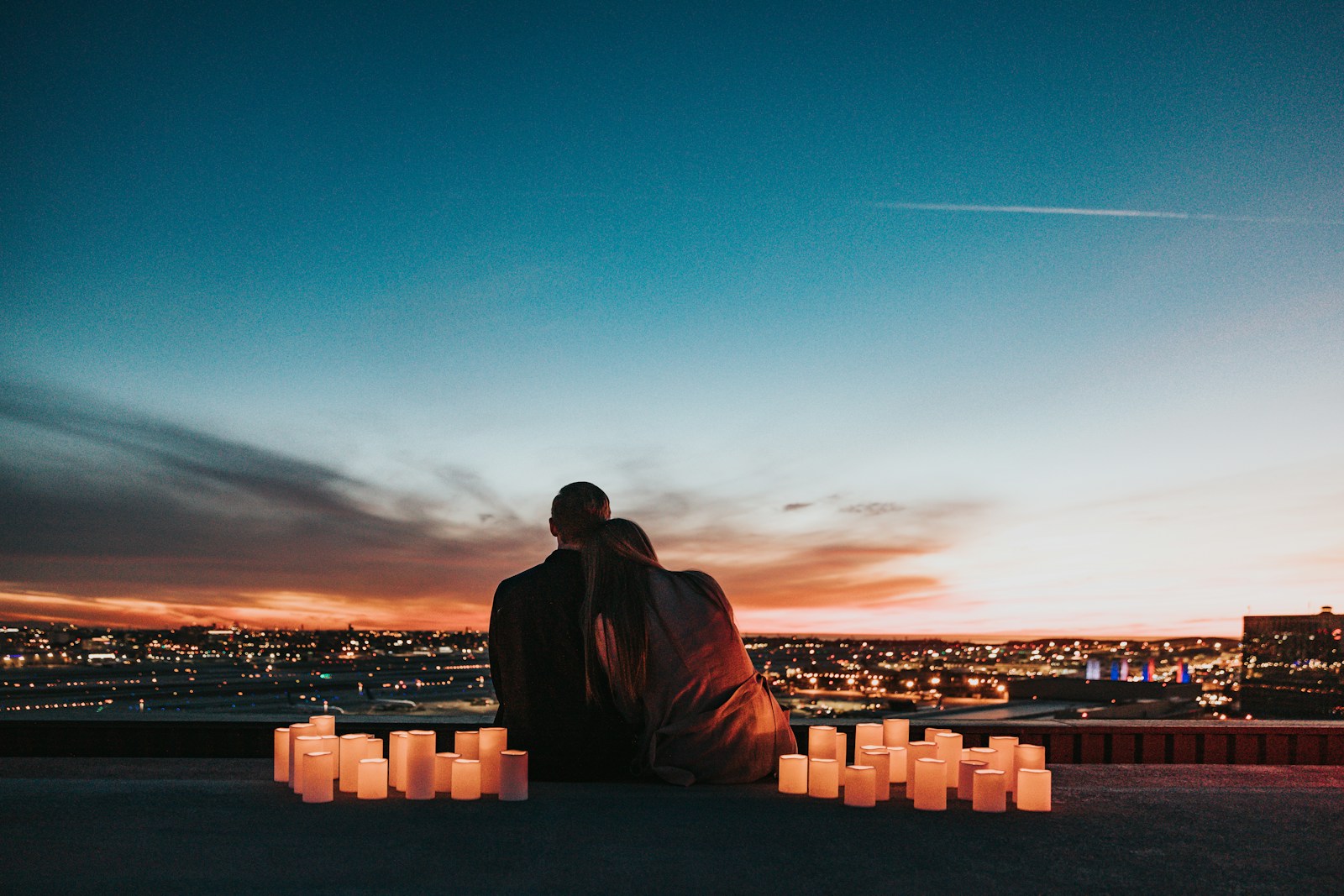 Two people sitting together behind glowing candles overlooking a city at night