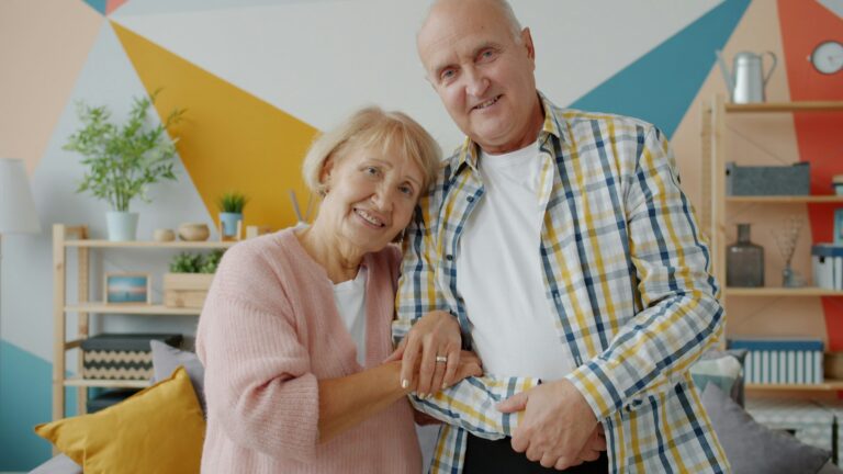 Elderly couple smiling and holding hands together in a warmly lit room
