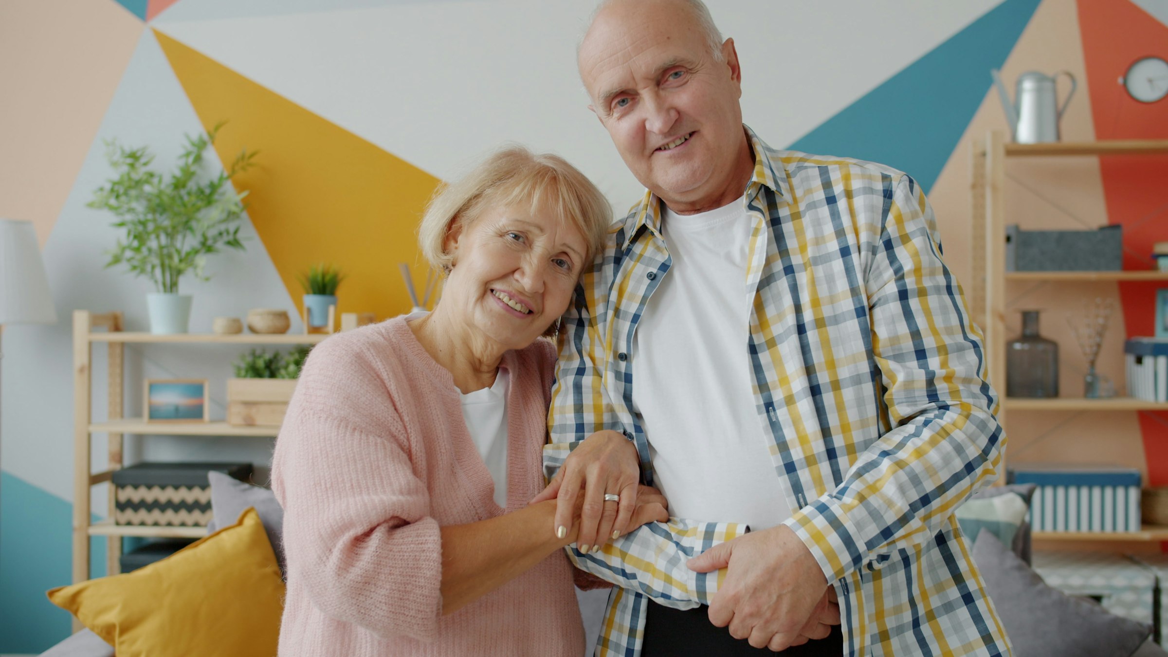 Elderly couple smiling and holding hands together in a warmly lit room