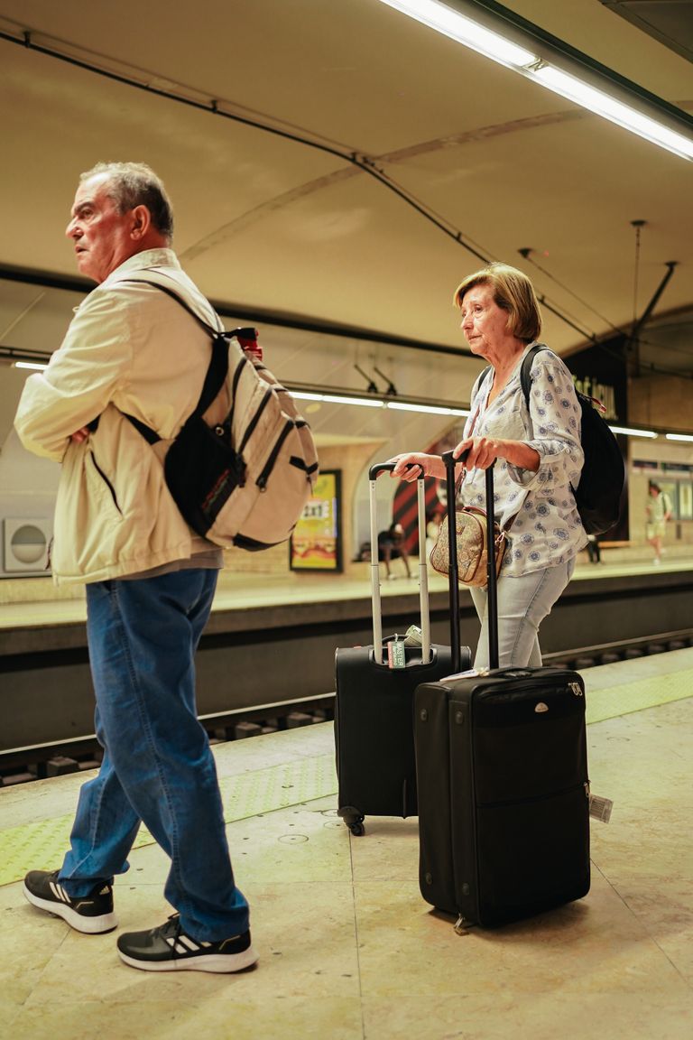 Elderly couple with luggage at a Lisbon subway platform, poised for travel adventure.