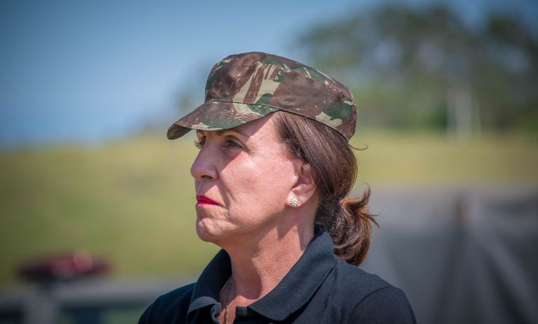 Elderly woman wearing camouflage cap in an outdoor military setting.