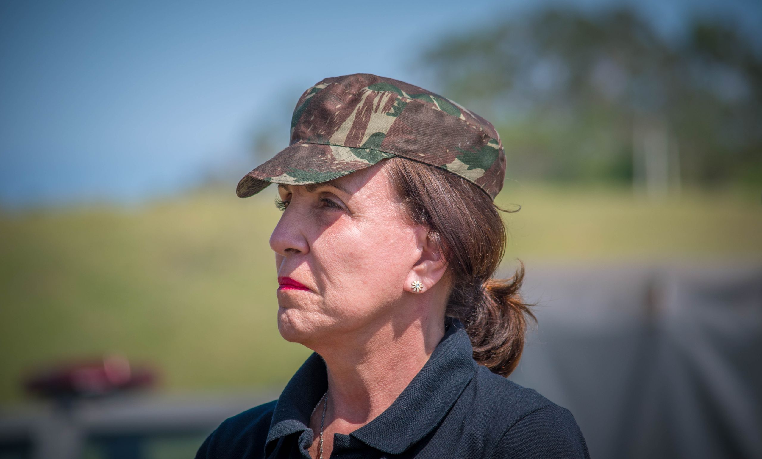 Elderly woman wearing camouflage cap in an outdoor military setting.
