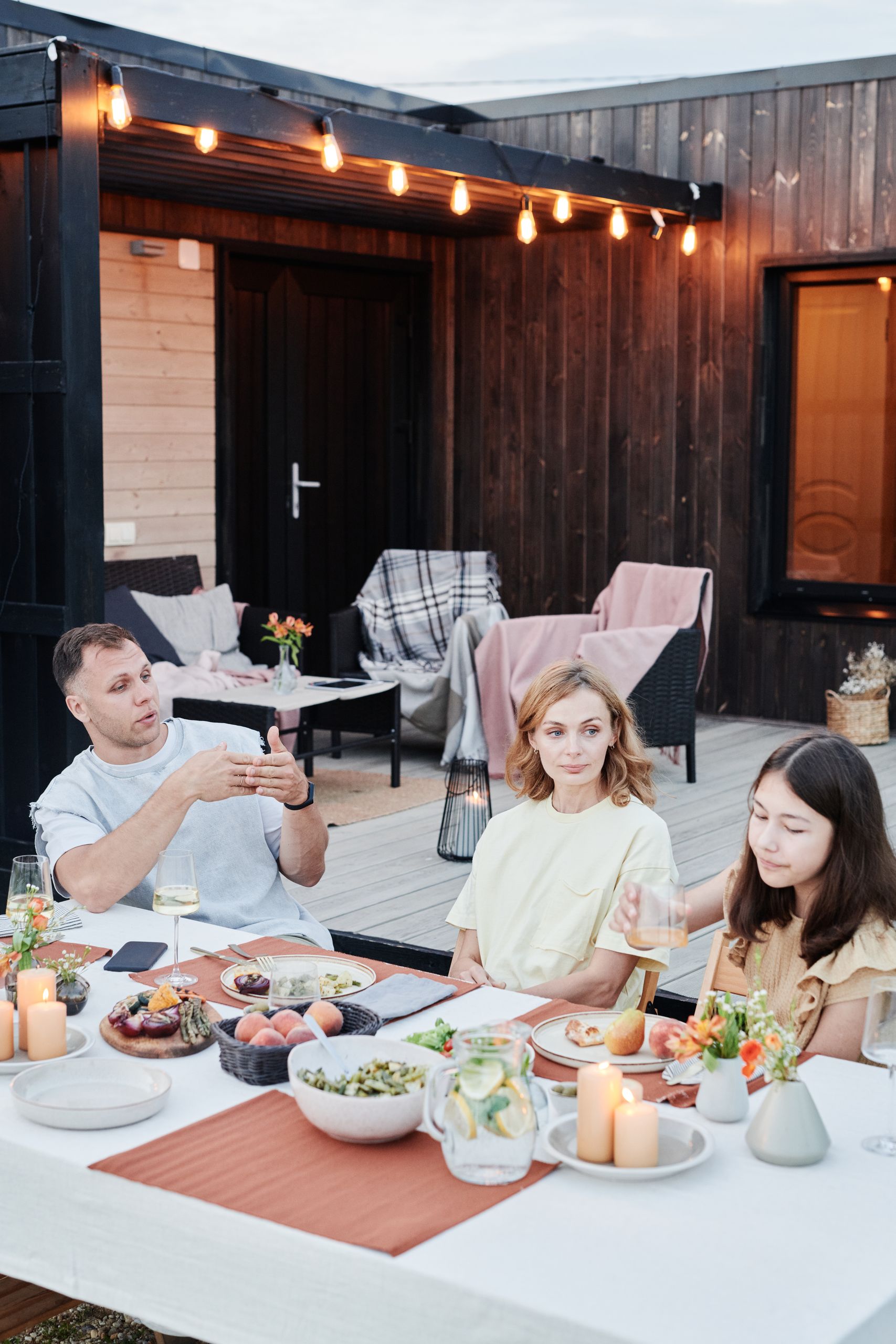 Family enjoying dinner outdoors with candles, food, and drinks on a summer evening.
