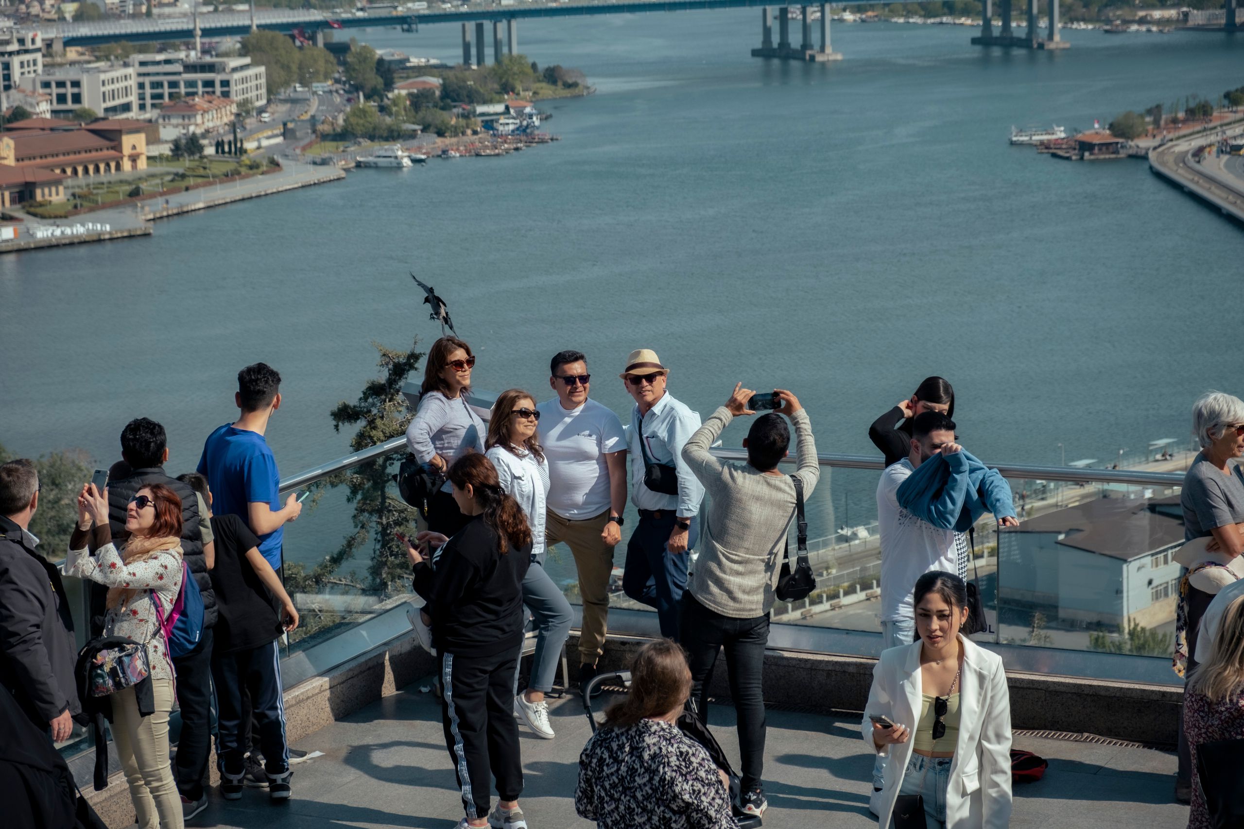 Group of tourists taking photos at a city overlook with a river and bridge in the background.