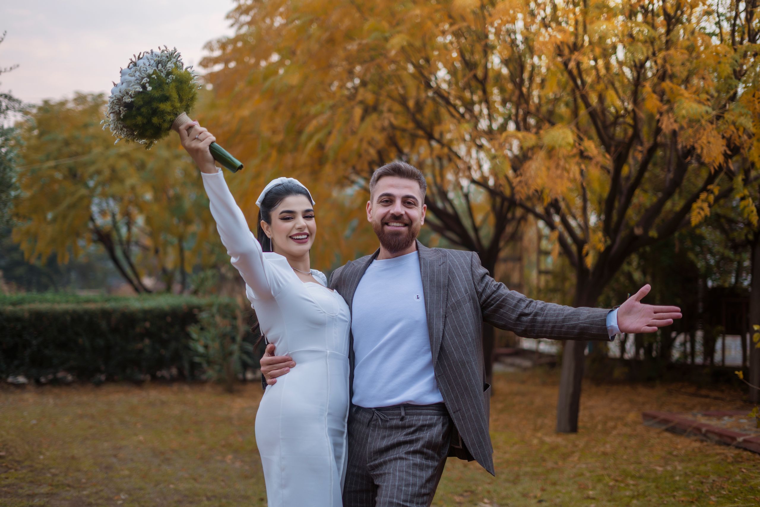 Happy bride and groom celebrating their autumn wedding outdoors with vibrant foliage.