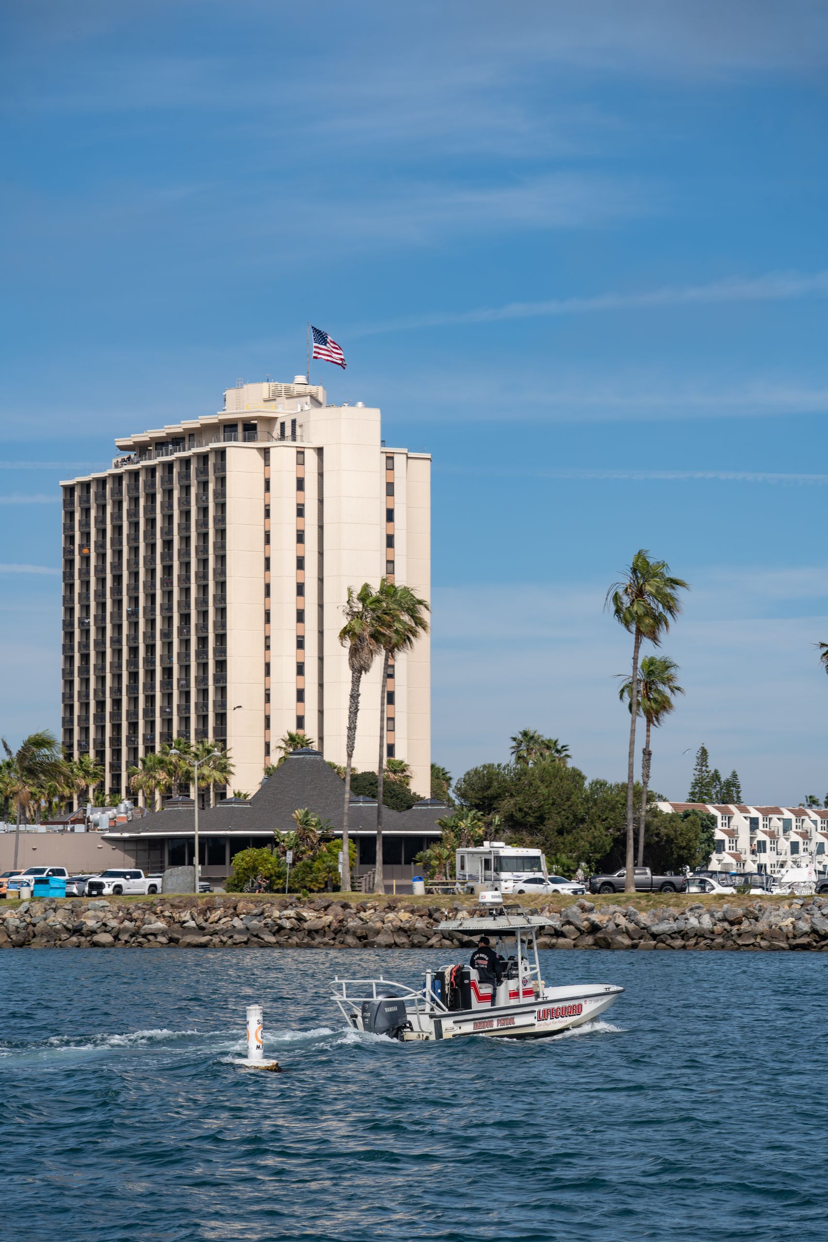 Lifeguard boat patrolling Mission Bay with a hotel and palm trees in San Diego.