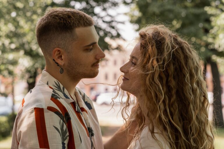 A couple standing close and making direct eye contact outdoors in dappled sunlight