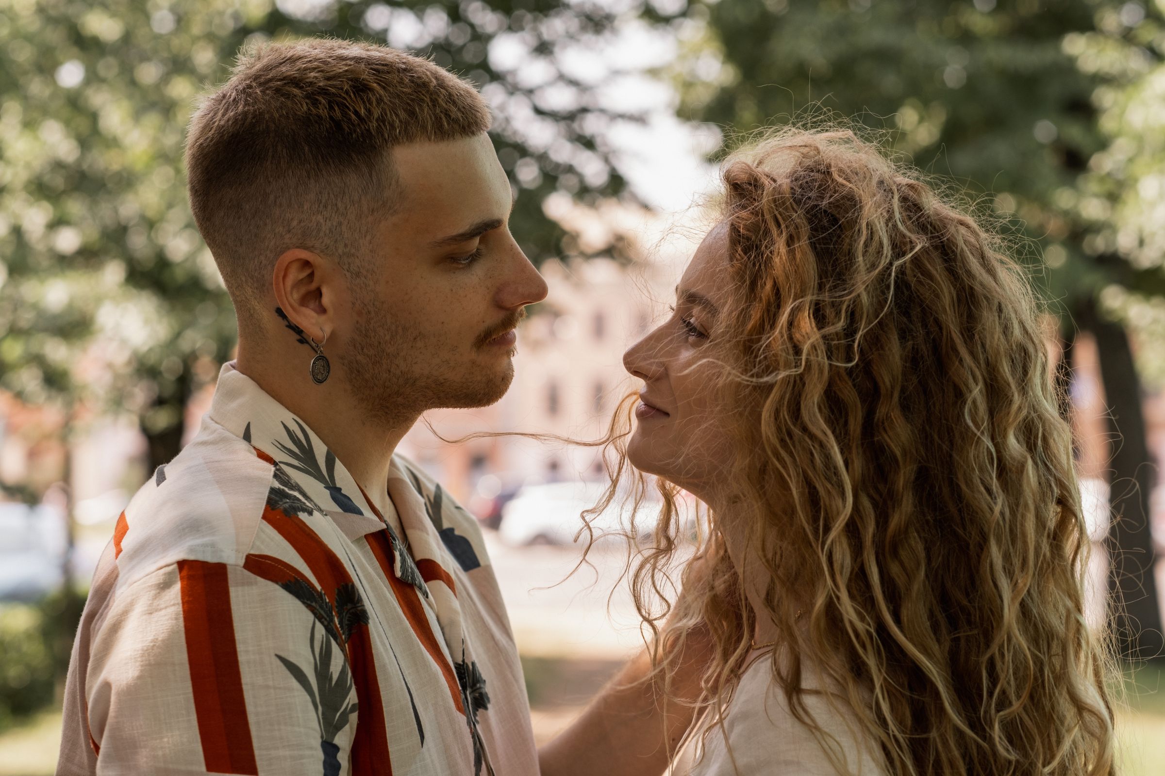 A couple standing close and making direct eye contact outdoors in dappled sunlight