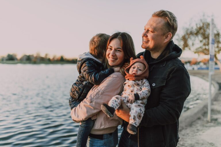 Parents and two young children sharing an affectionate moment together by a lake at golden hour