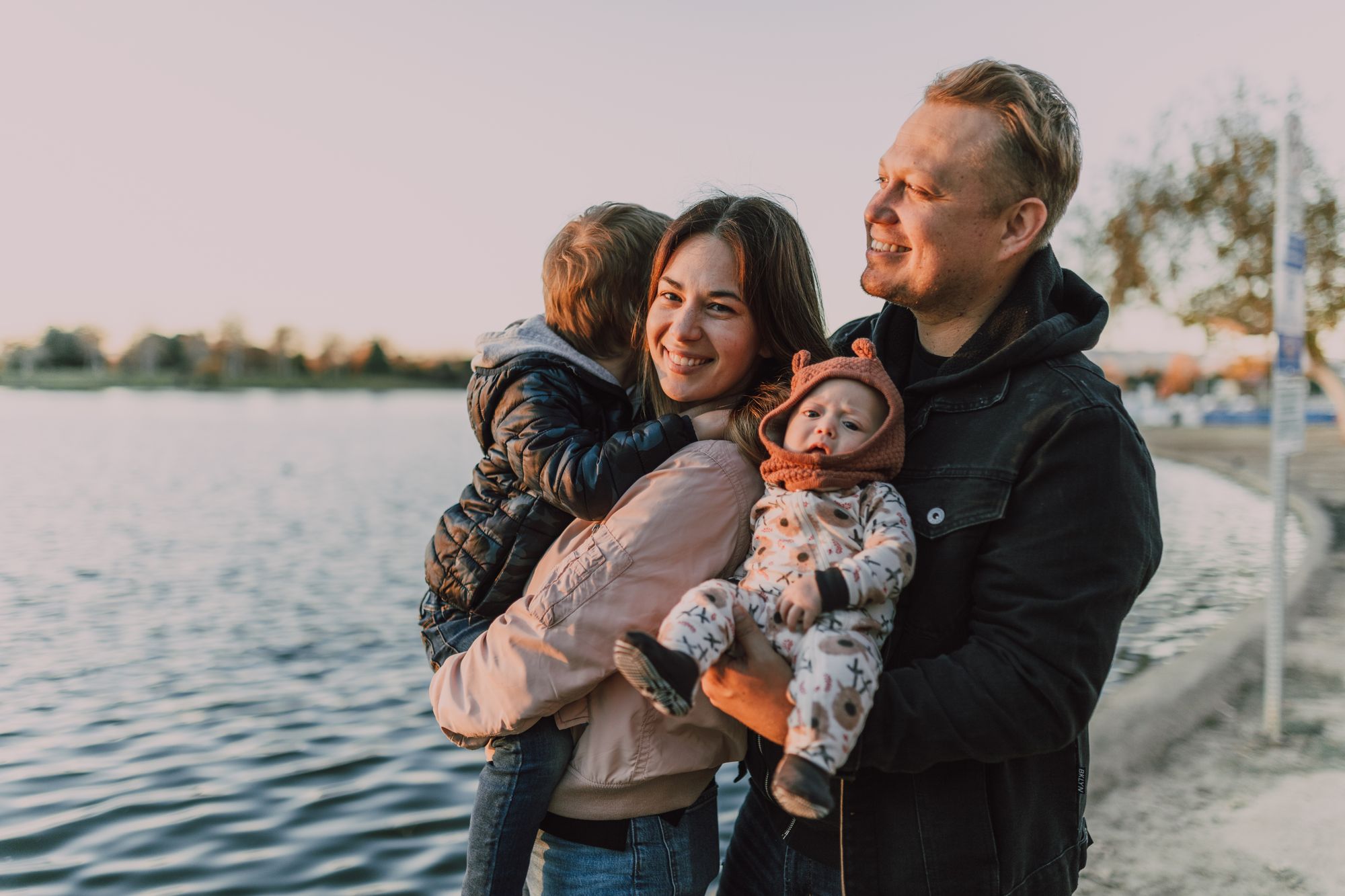 Parents and two young children sharing an affectionate moment together by a lake at golden hour
