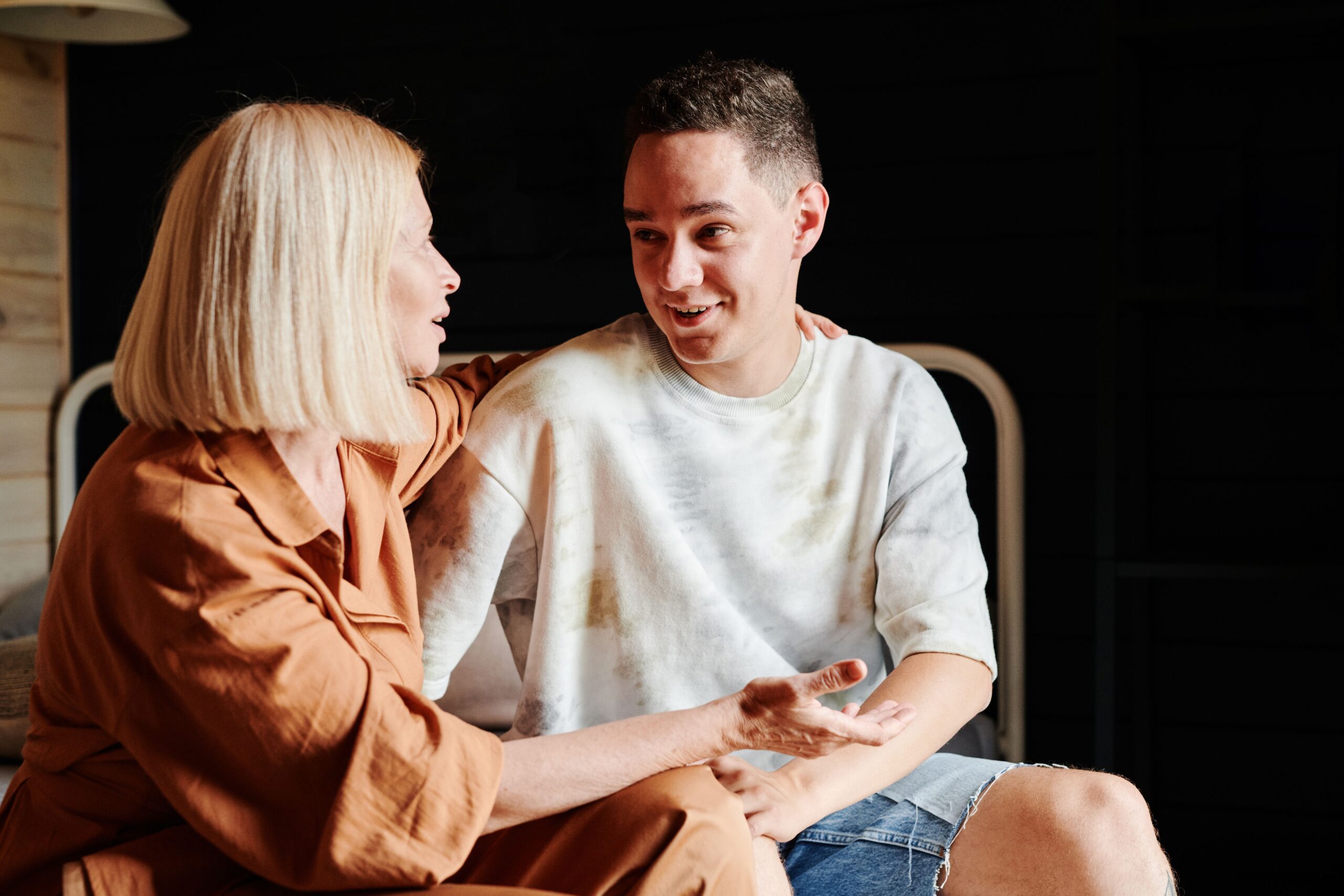 A mother and her adult son sitting side by side at home, having a warm, unhurried conversation