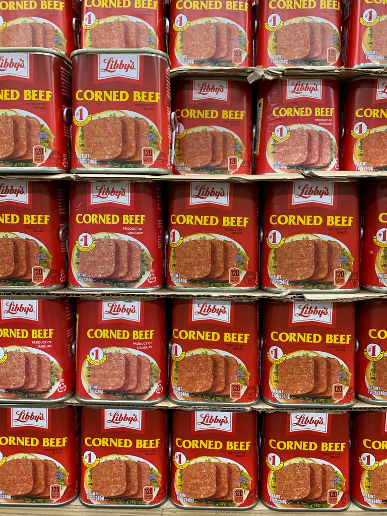 Multiple cans of corned beef neatly organized on supermarket shelves.
