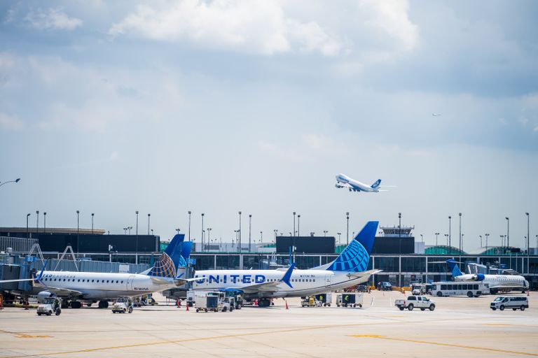 Multiple United Airlines aircraft on the tarmac at an airport with one taking off under a partly cloudy sky.