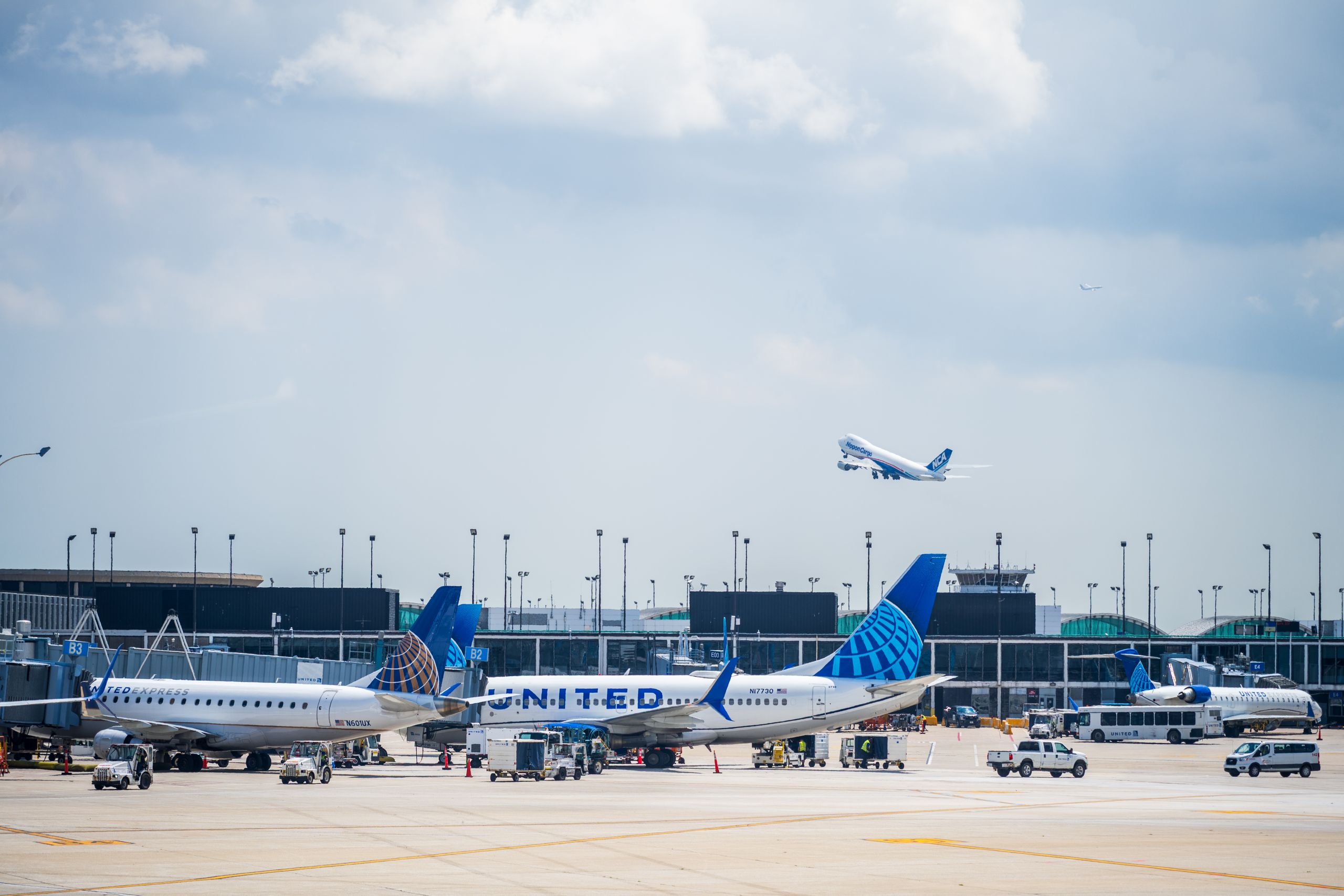 Multiple United Airlines aircraft on the tarmac at an airport with one taking off under a partly cloudy sky.