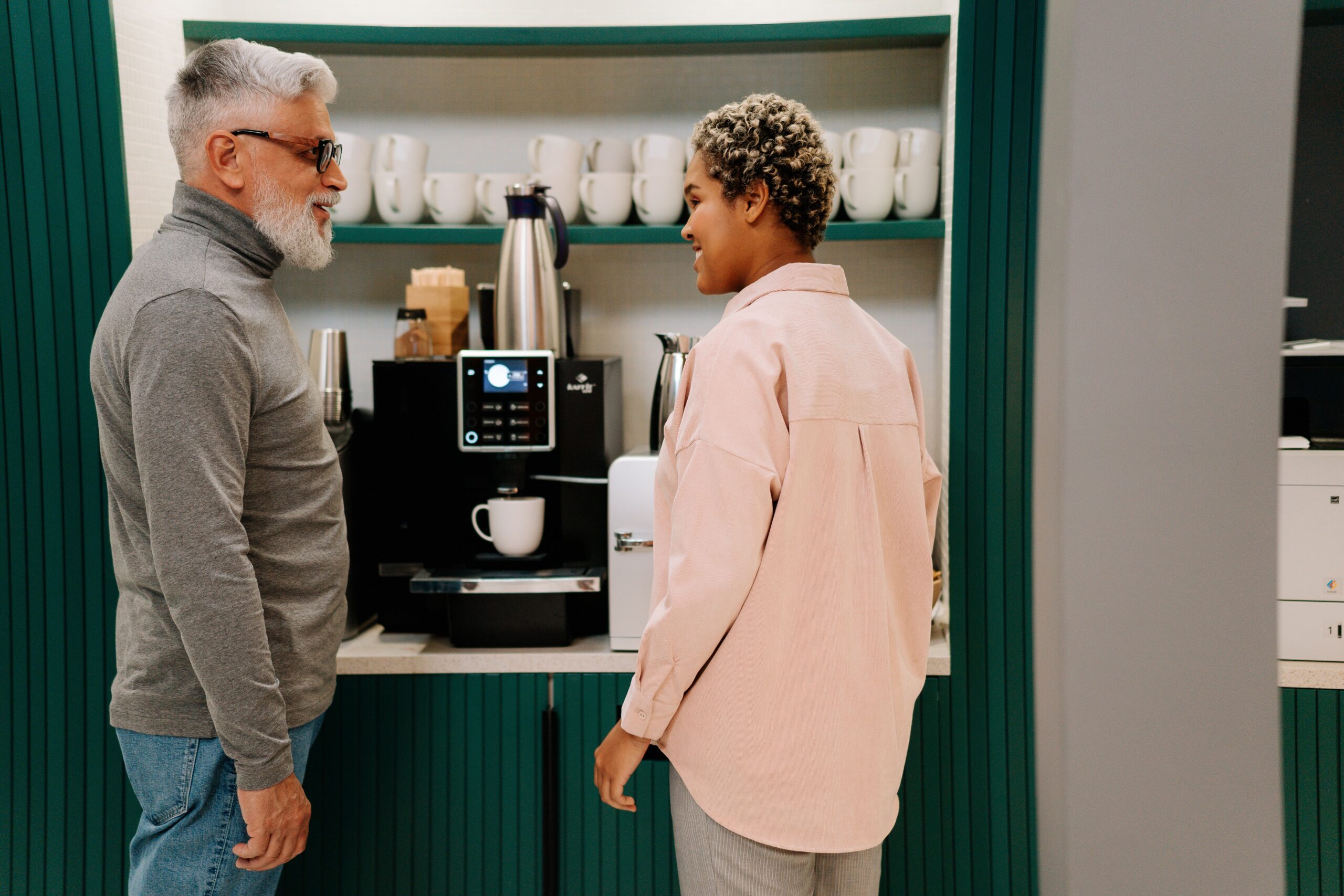 A man and woman having a quiet conversation near an office coffee machine
