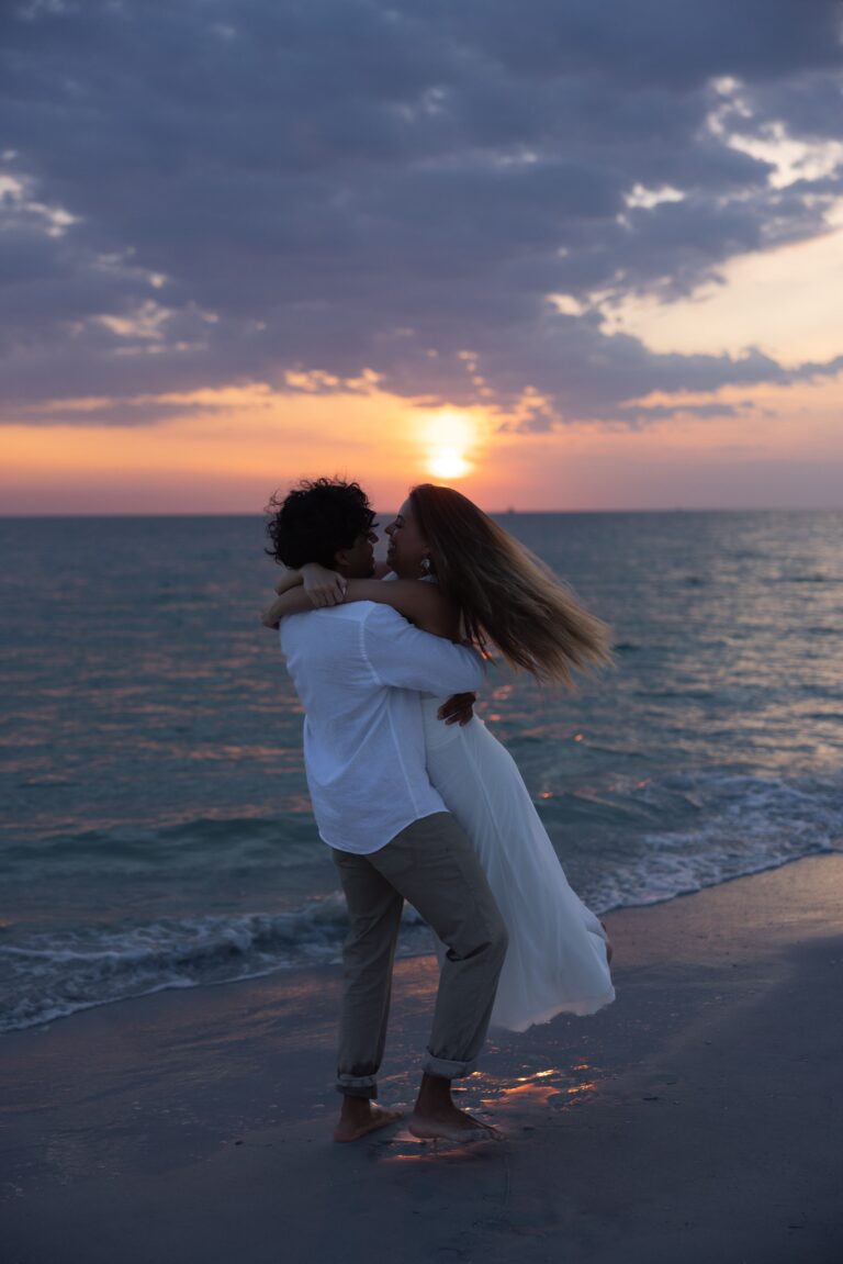 A couple embracing on a beach at golden hour, silhouetted against the ocean and setting sun