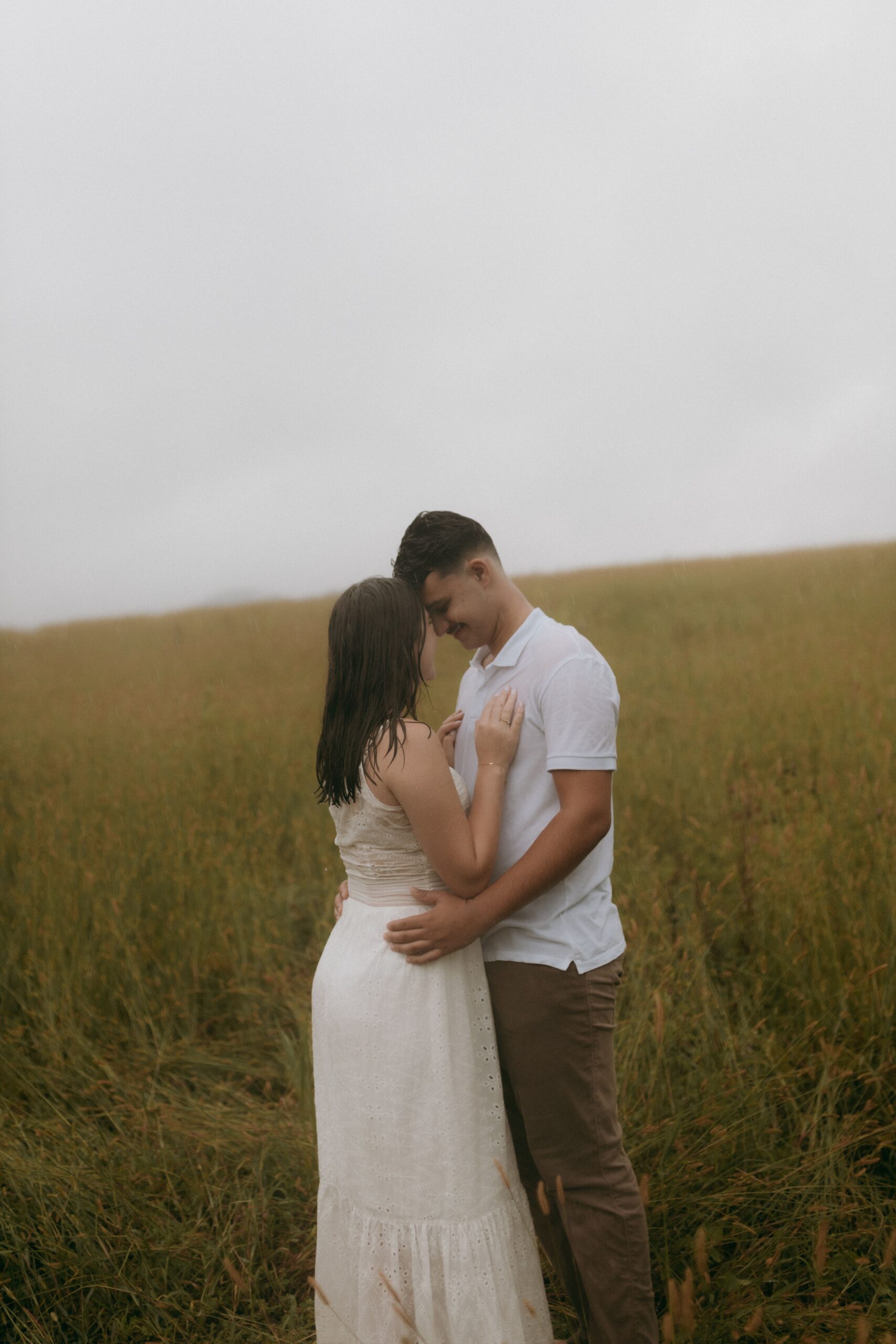 Two people embracing closely in an open grassy field under soft, misty morning light
