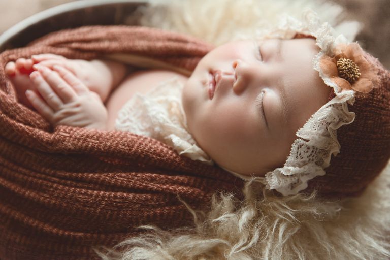 Peaceful baby sleeping in a basket, wrapped in a soft knitted blanket with a floral headband.