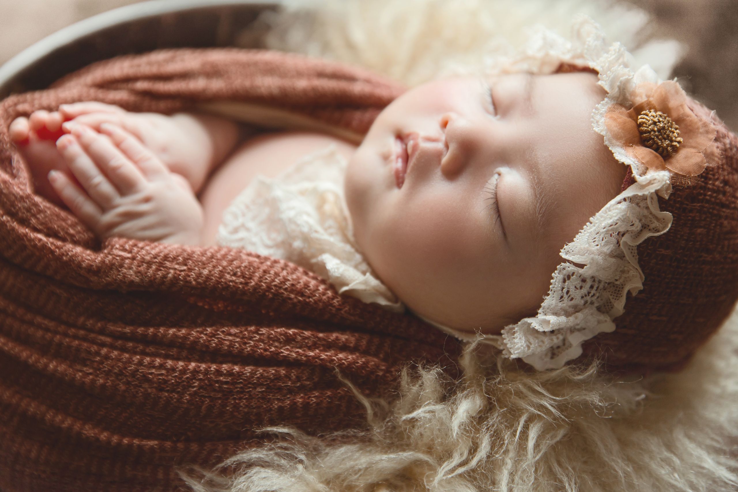 Peaceful baby sleeping in a basket, wrapped in a soft knitted blanket with a floral headband.