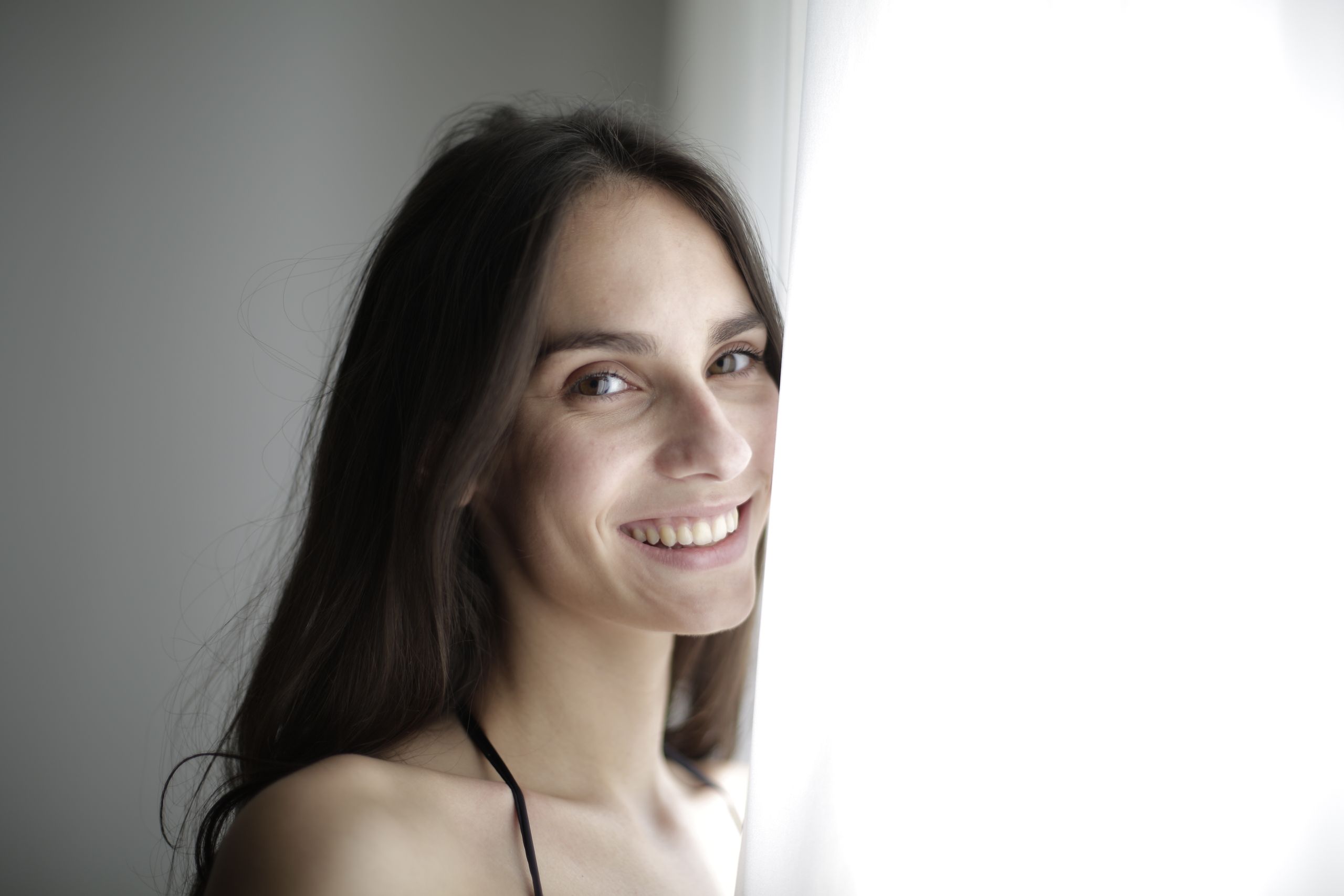 Portrait of a smiling woman with brunette hair in soft natural light, exuding happiness and warmth.