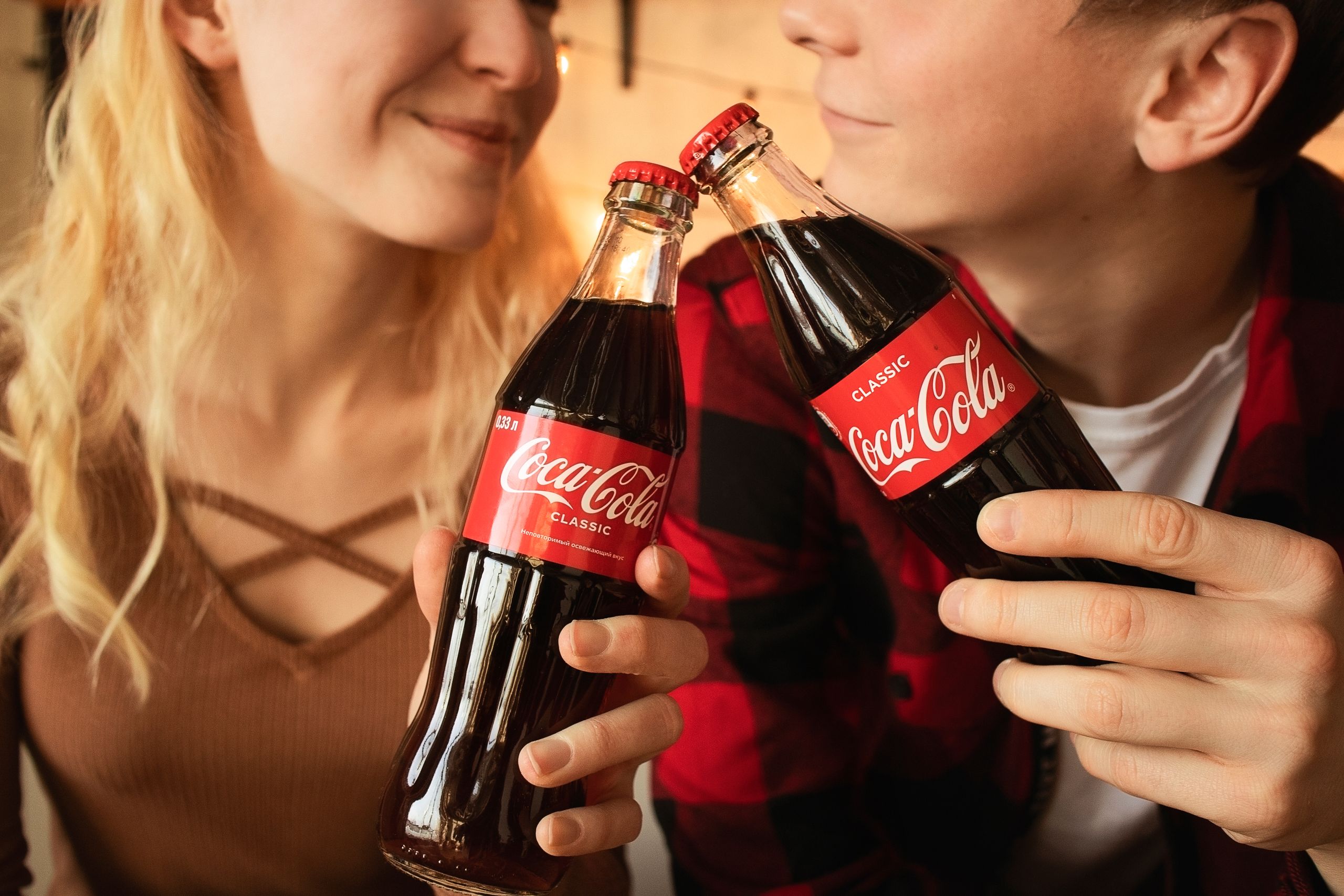Smiling couple toasting with classic Coca-Cola glass bottles.