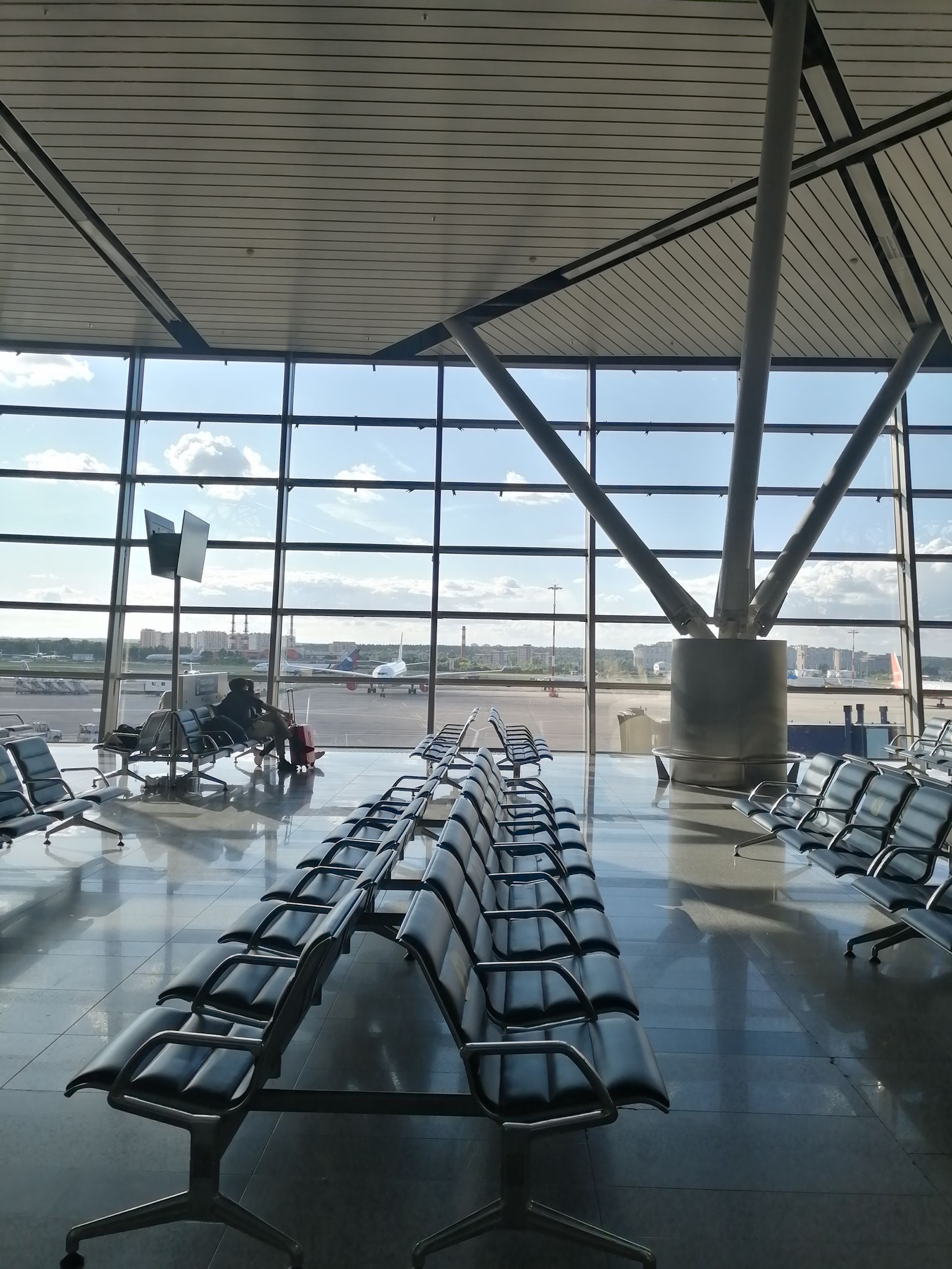 Spacious seating area in a modern airport terminal with large windows overlooking the runway.