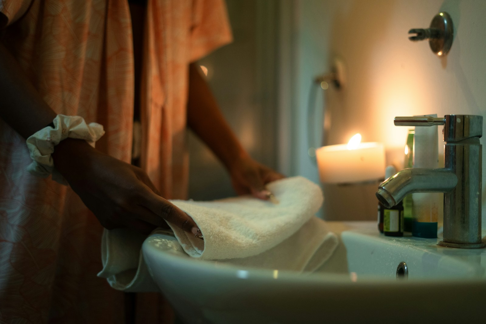 Woman folding a towel by a sink with candle.