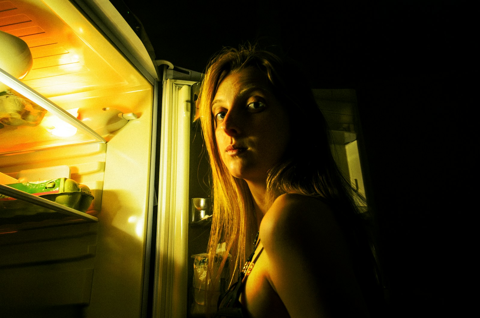 a woman looking into an open refrigerator at night