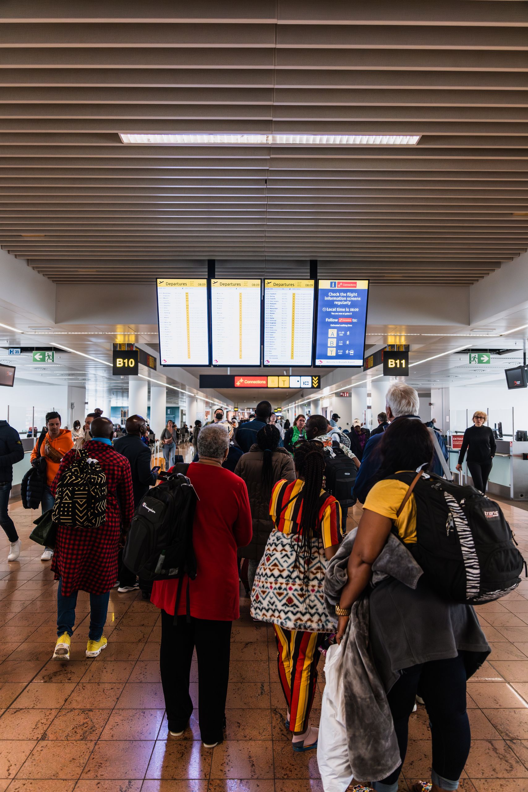 Travelers lining up in a busy airport terminal with baggage under flight information screens.