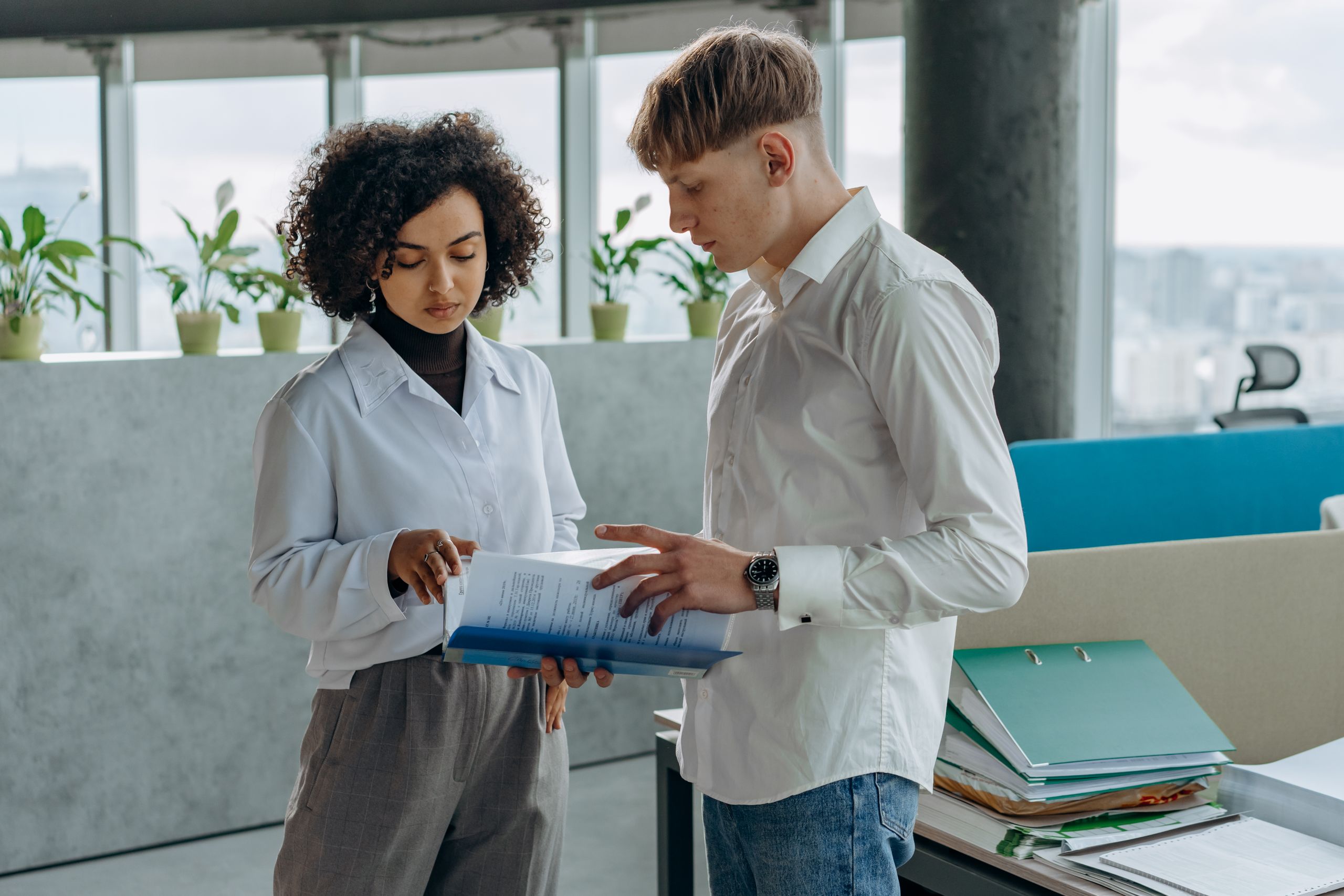 Two business colleagues examining documents in a modern office setting with city views.