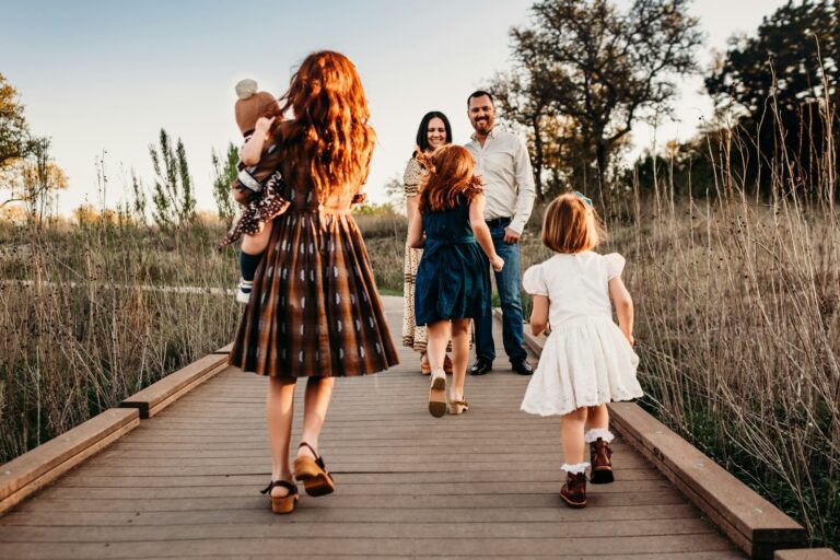 A family walking along a wooden boardwalk in a field during golden hour