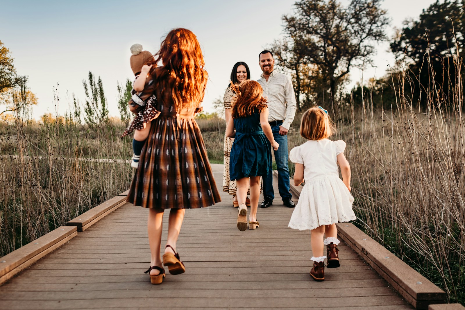 A family walking along a wooden boardwalk in a field during golden hour
