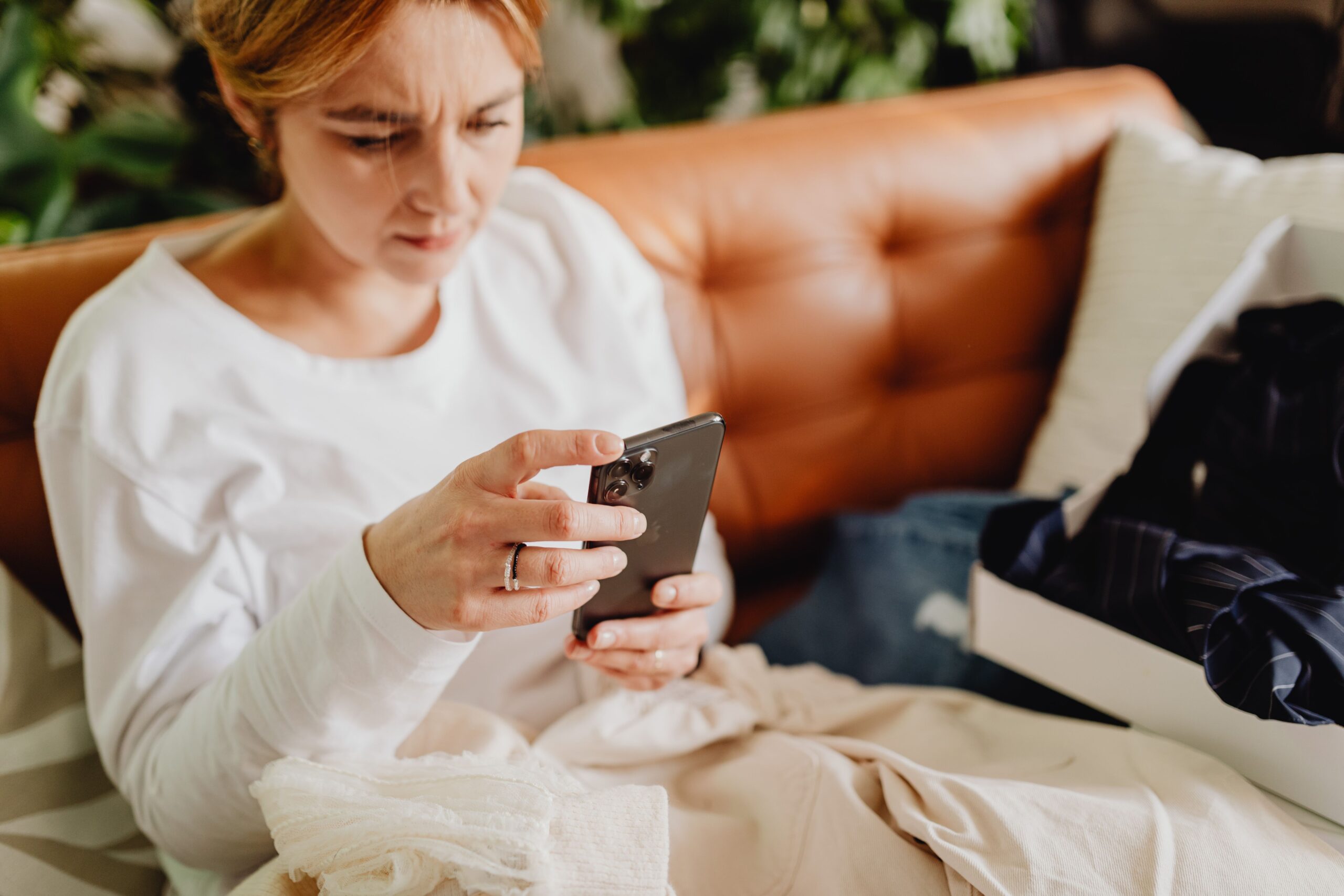 A woman sitting alone on a couch at home, scrolling through her phone