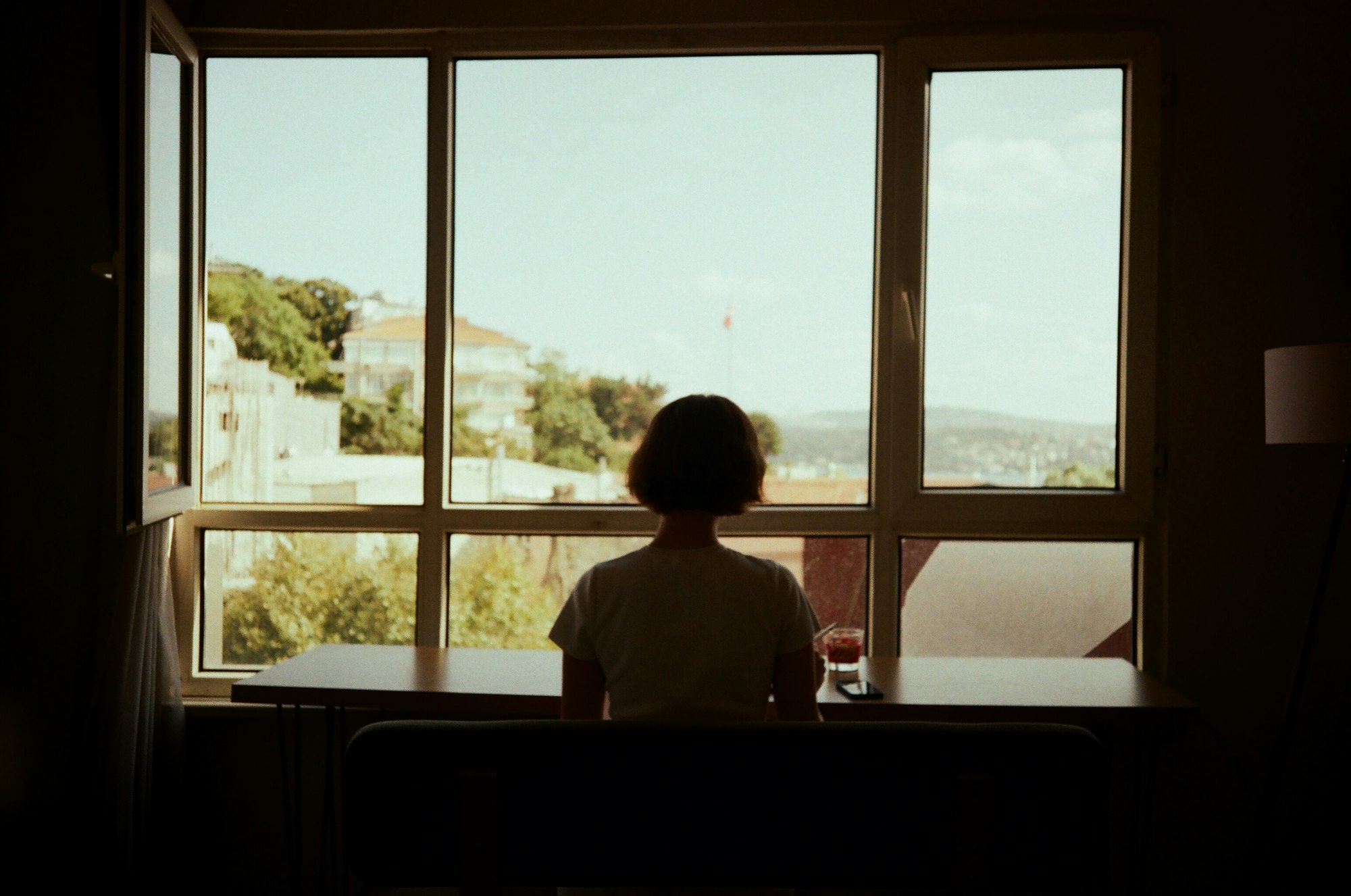 A woman sits alone at a table, gazing out a window in quiet solitude