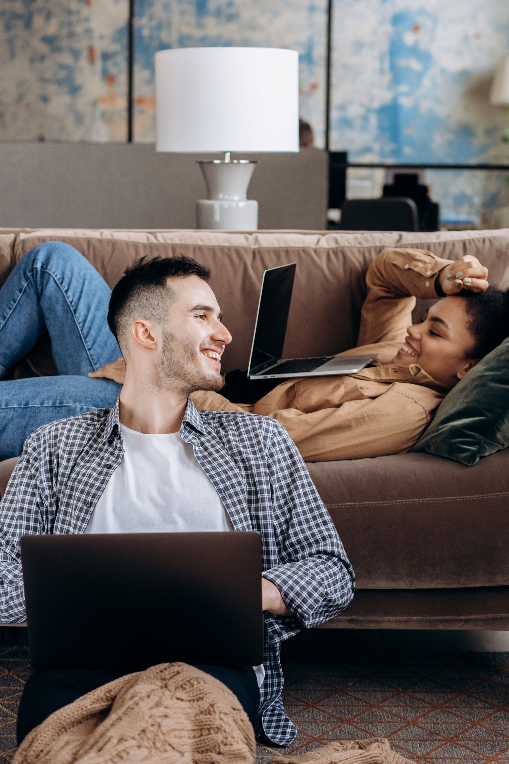 Young couple enjoys remote work from home setting, using laptops on a cozy couch.