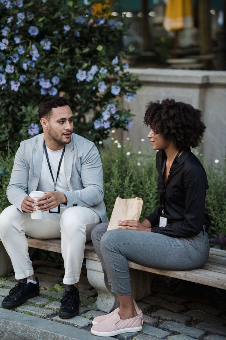 A relaxed couple having a conversation on a park bench surrounded by lush flowers.