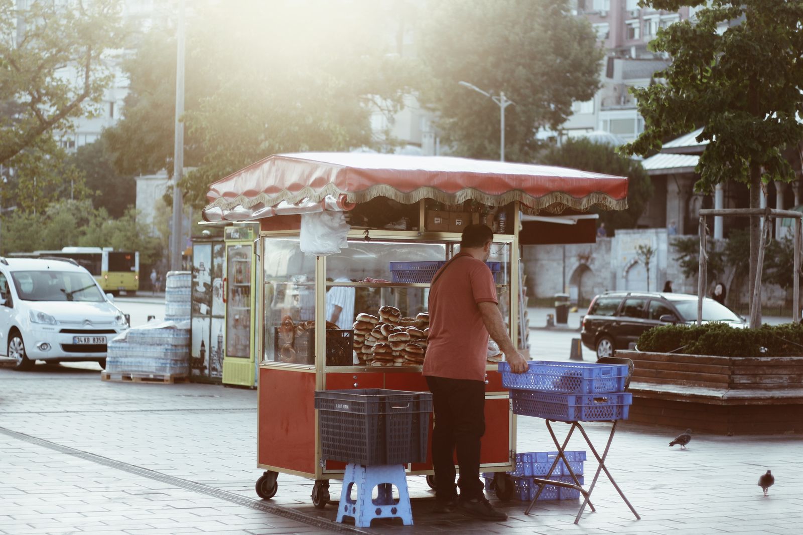 Street vendor sells bagels at a morning stall in the city with sunlight filtering through.