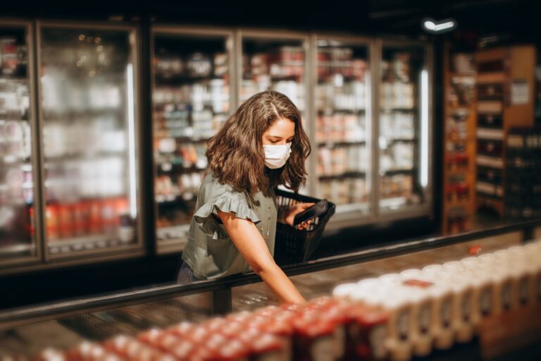 Woman wearing a mask shopping for groceries in a supermarket aisle.