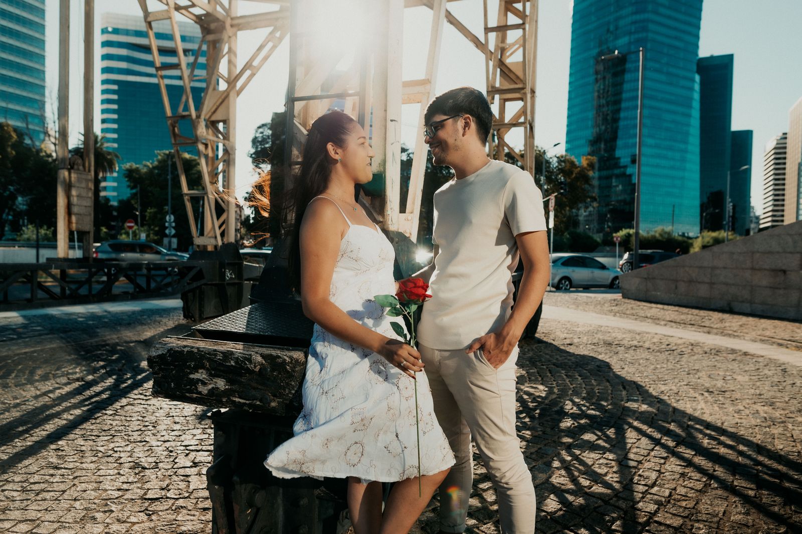 A romantic couple sharing a moment outdoors in Buenos Aires, holding a red rose under the city skyline.
