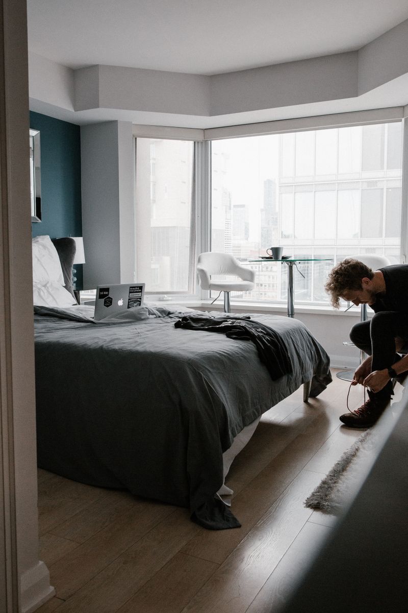 A person tying shoes in a well-designed city apartment with laptop and window view.