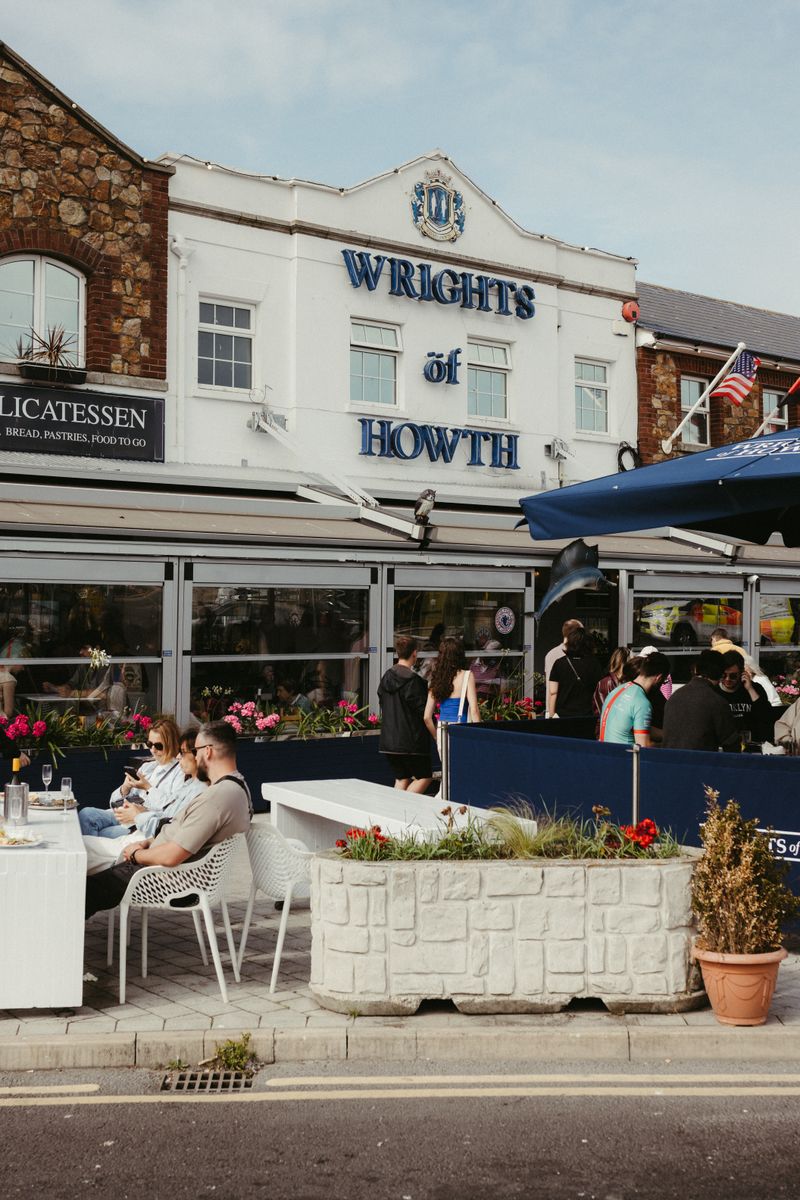 Lively outdoor dining scene at Wrights of Howth, Dublin, Ireland with people enjoying sunny weather.