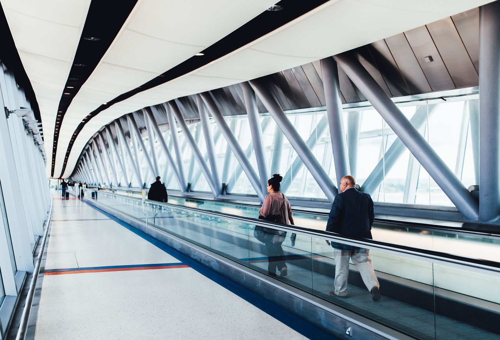 Travelers walking through a bright modern airport corridor with glass walls.