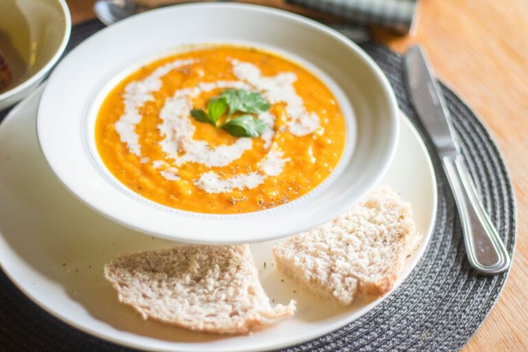 Delicious creamy pumpkin soup garnished with cream and parsley, served with sliced bread.