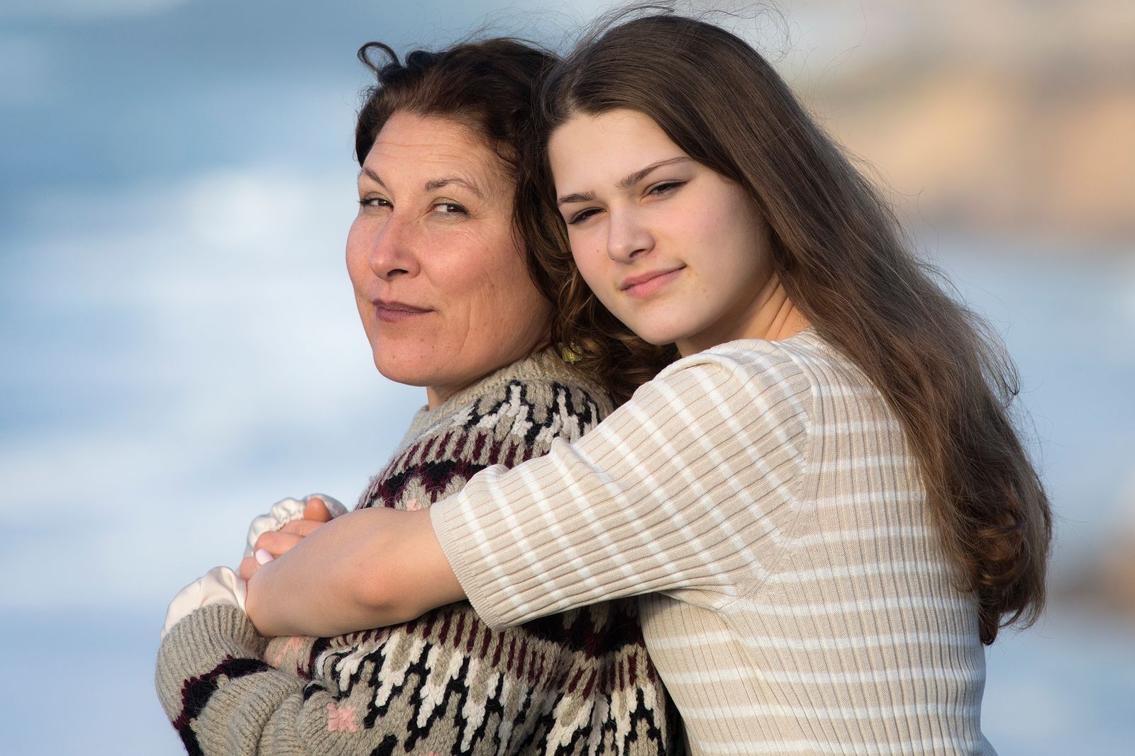 A mother and daughter share a warm embrace at the beach, depicting familial love and connection.