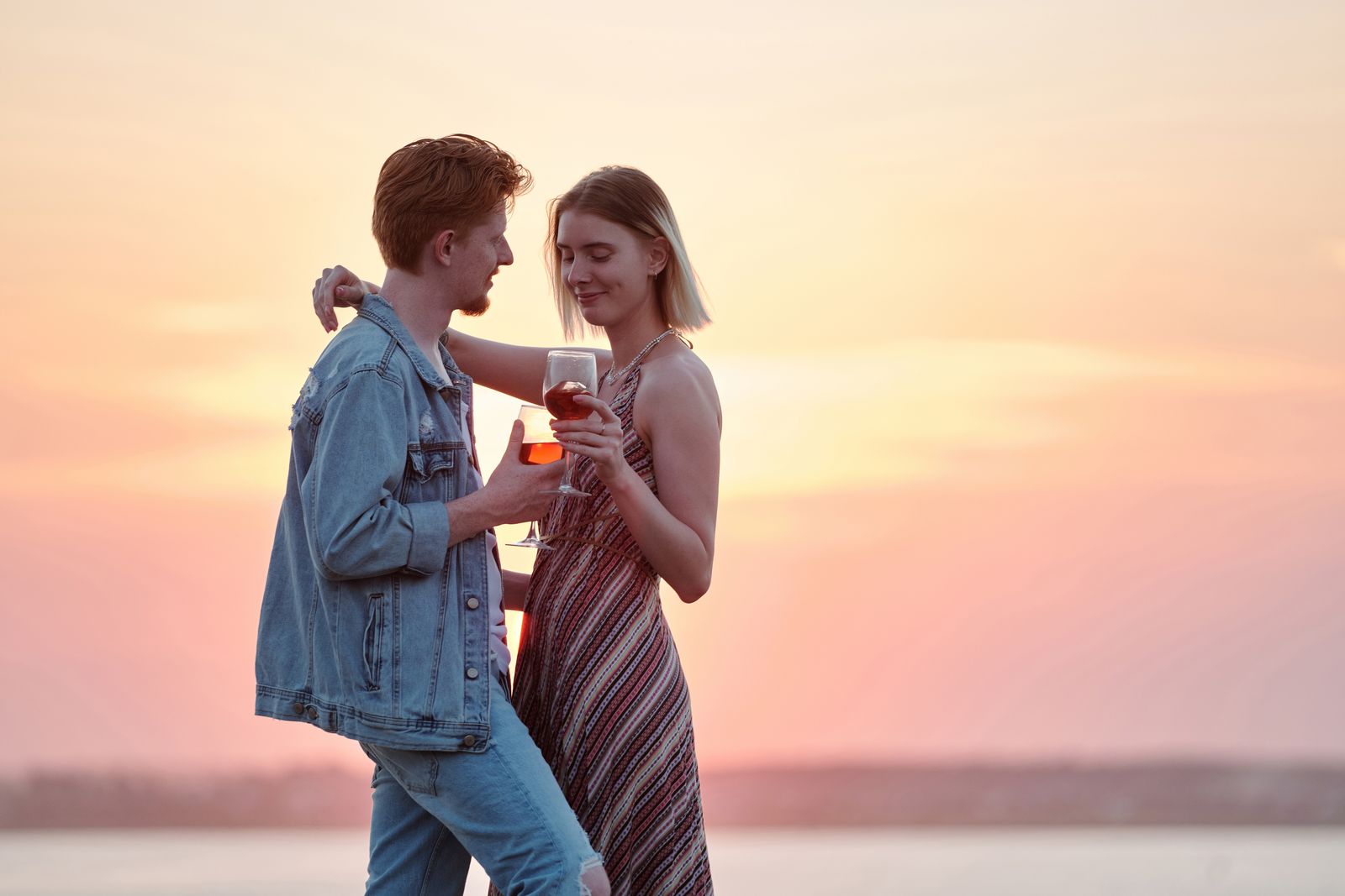 A loving couple enjoys a sunset together, holding wine glasses and embracing affectionately.