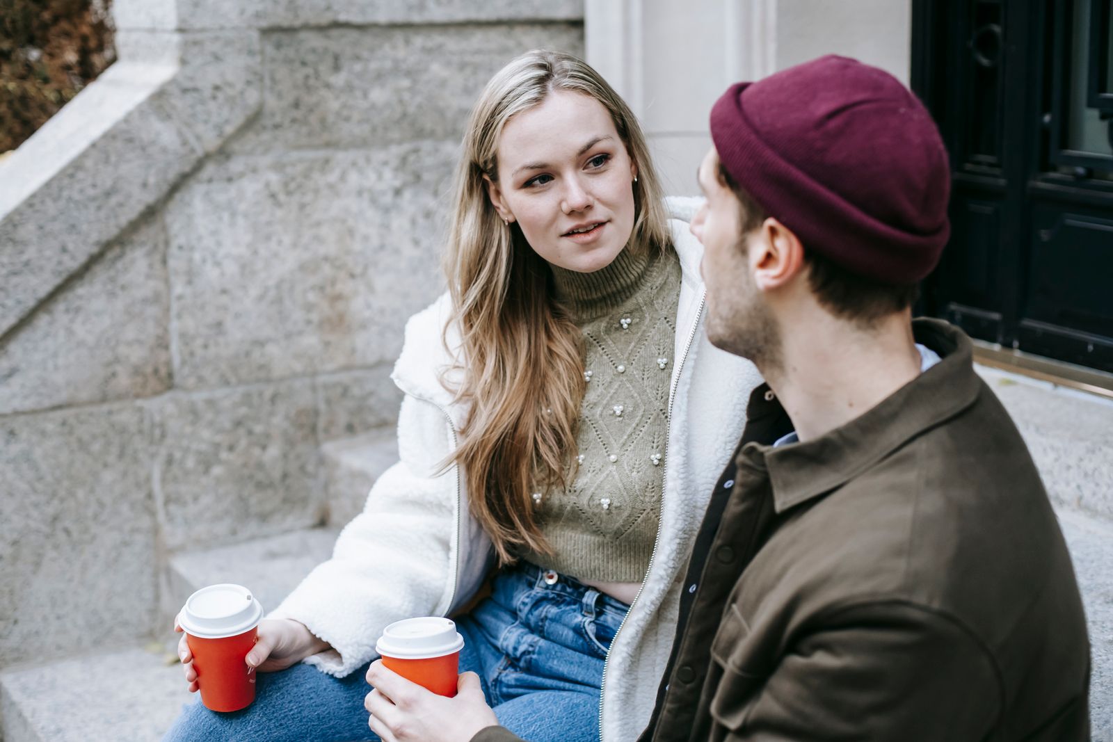 Man and woman talking sitting on steps outside house and having hot beverage in paper cups