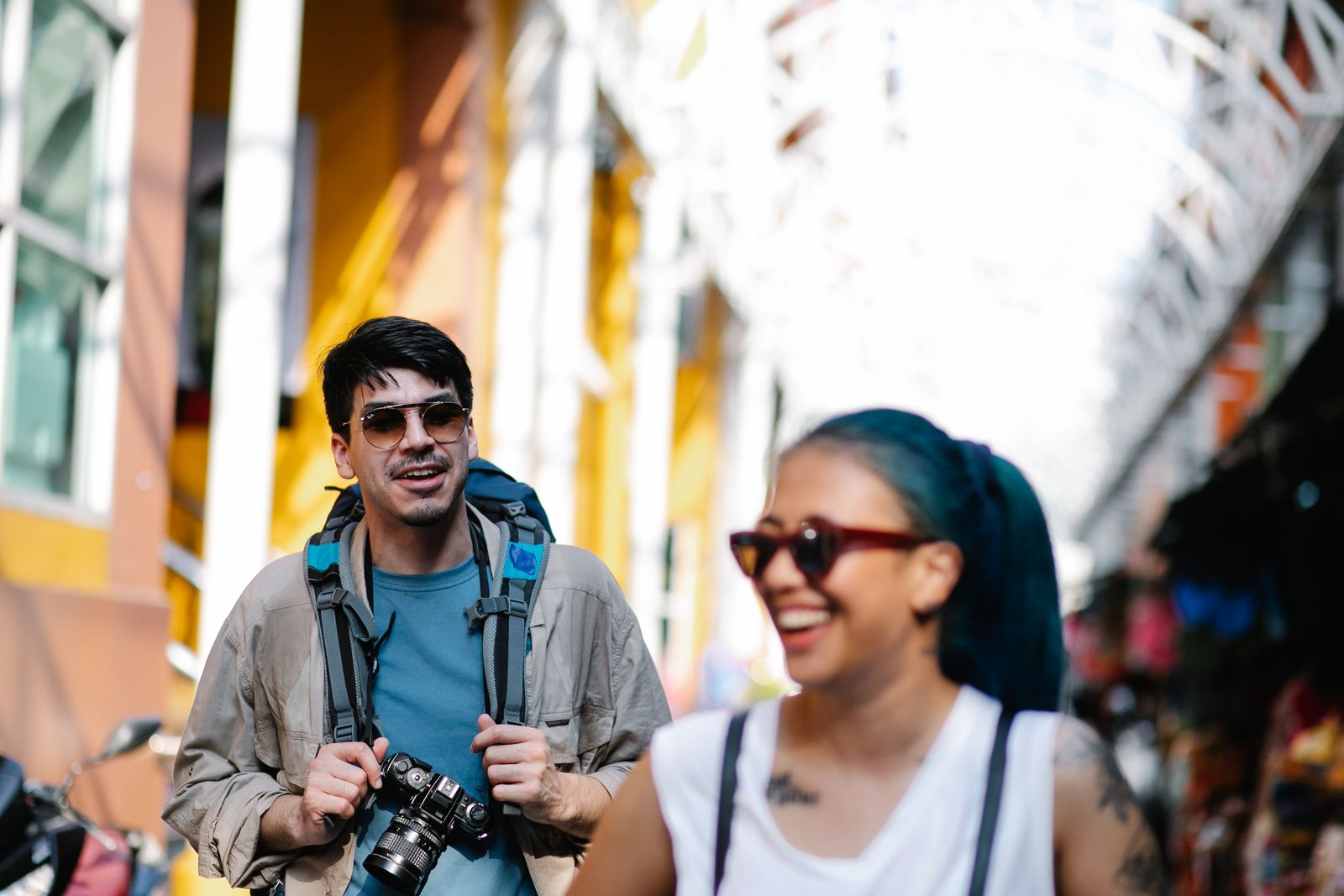 Joyful tourists walking through a colorful street market, capturing memories.